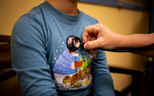  A child sits in the school clinic and the nurse checks him with a stethoscope.